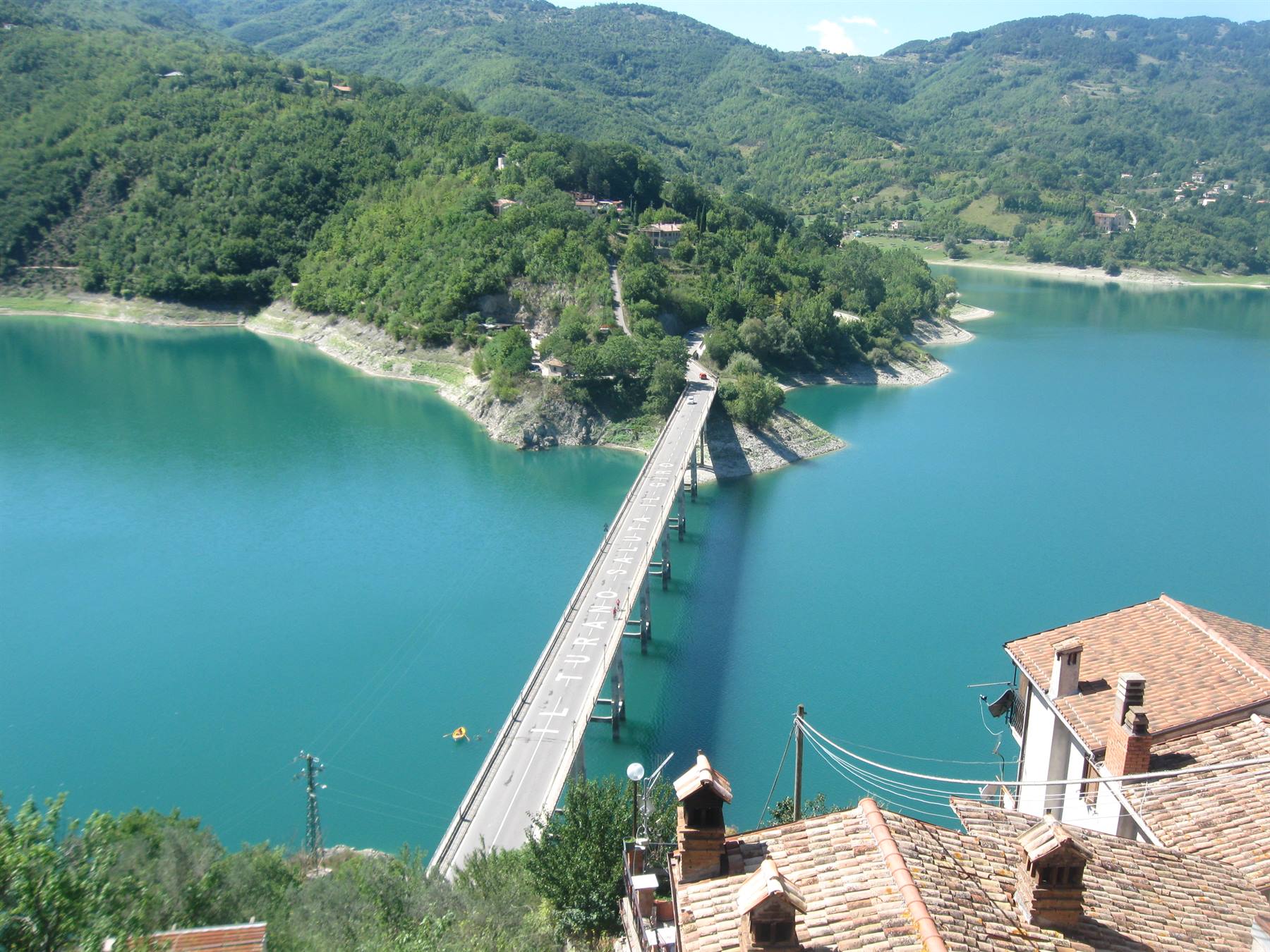 Ponte che attraversa il lago turchese di Turano tra case con tetti in cotto
