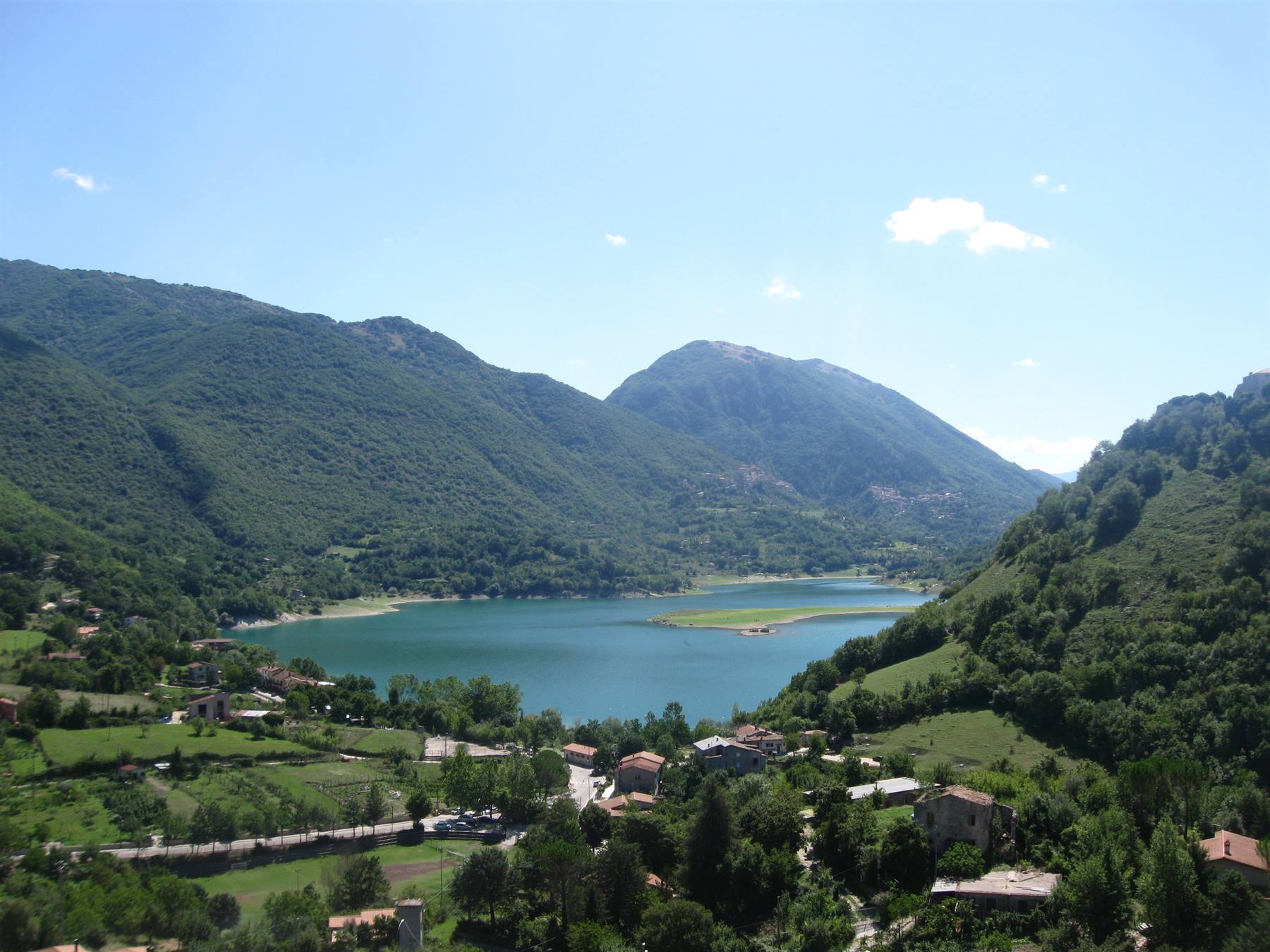 Lago di Scanno circondato da monti verdi, case e tetti sotto cielo azzurro