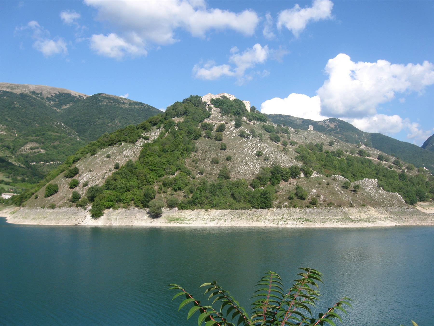 Lago del Turano: acque verdi ai piedi della collina boscosa con resti del castello