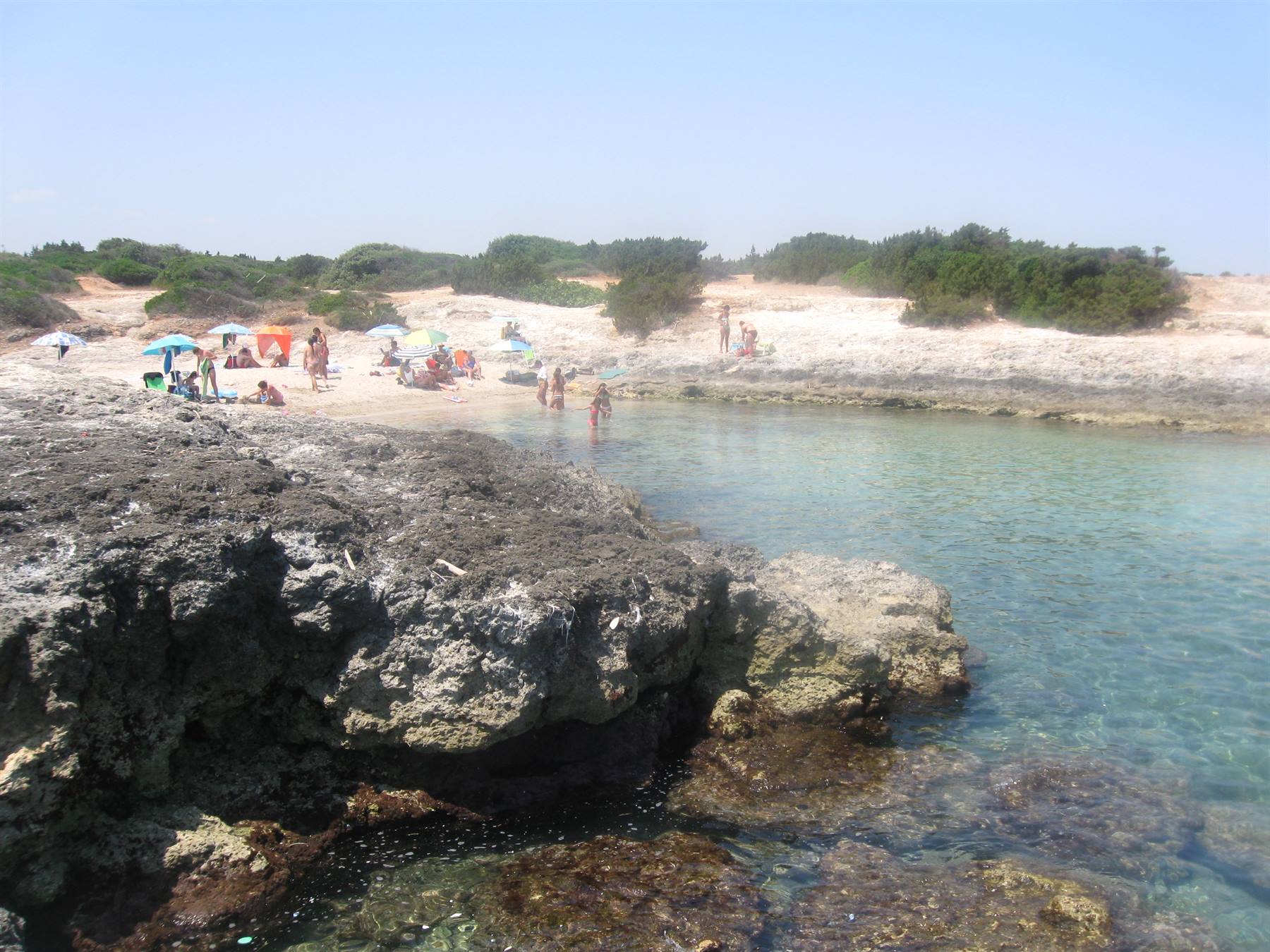 Bagnanti tra scogli bianchi e acqua trasparente, ombrelloni sulla spiaggetta
