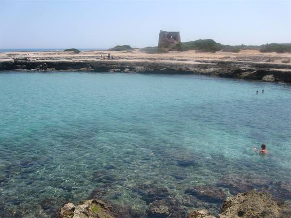 Swimmer in turquoise water among rocks, old coastal tower on the shore