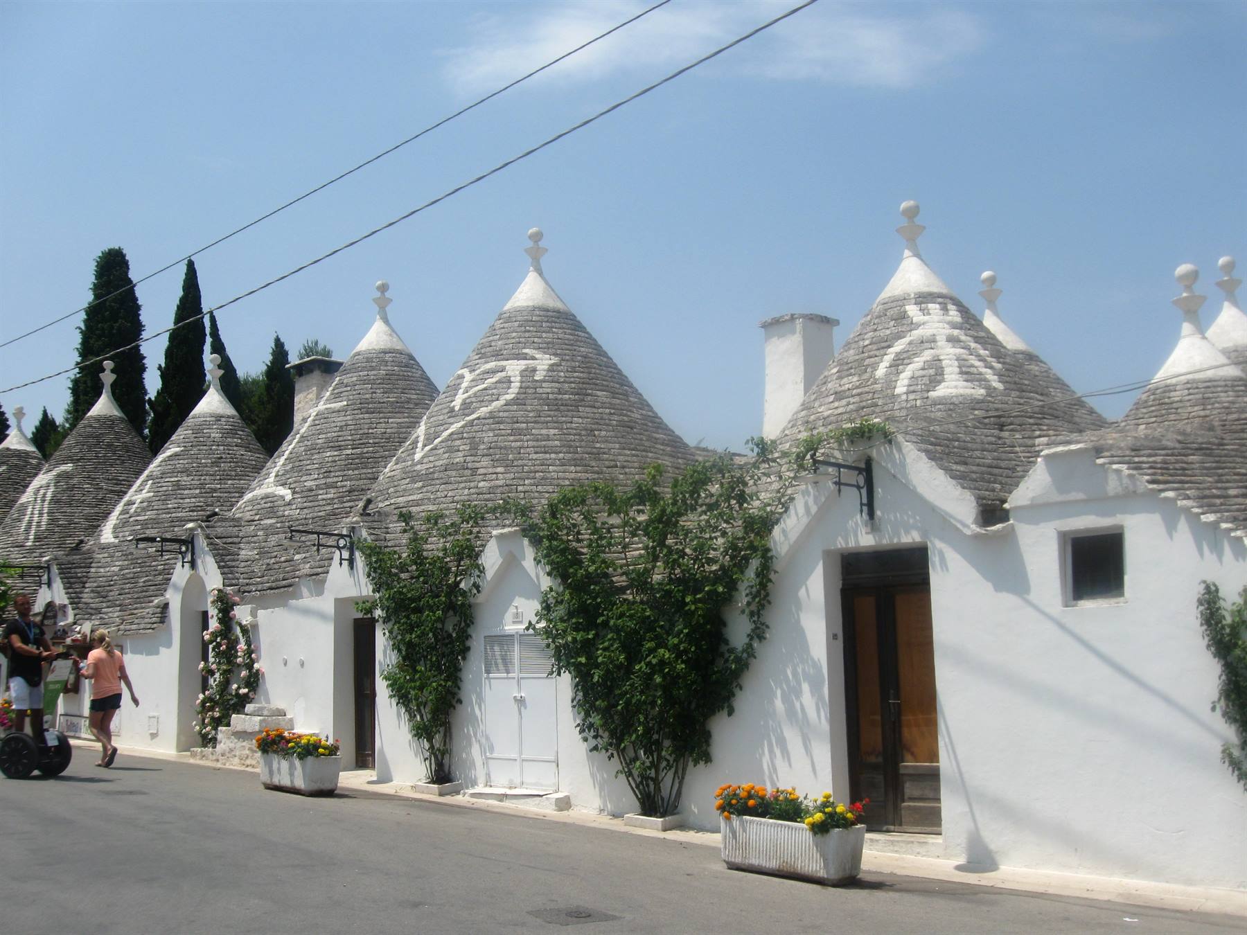 I trulli di Alberobello, tetti conici di pietra con simboli bianchi, turisti lungo la via