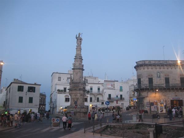 Ostuni, square with Sant'Oronzo column among white houses at dusk