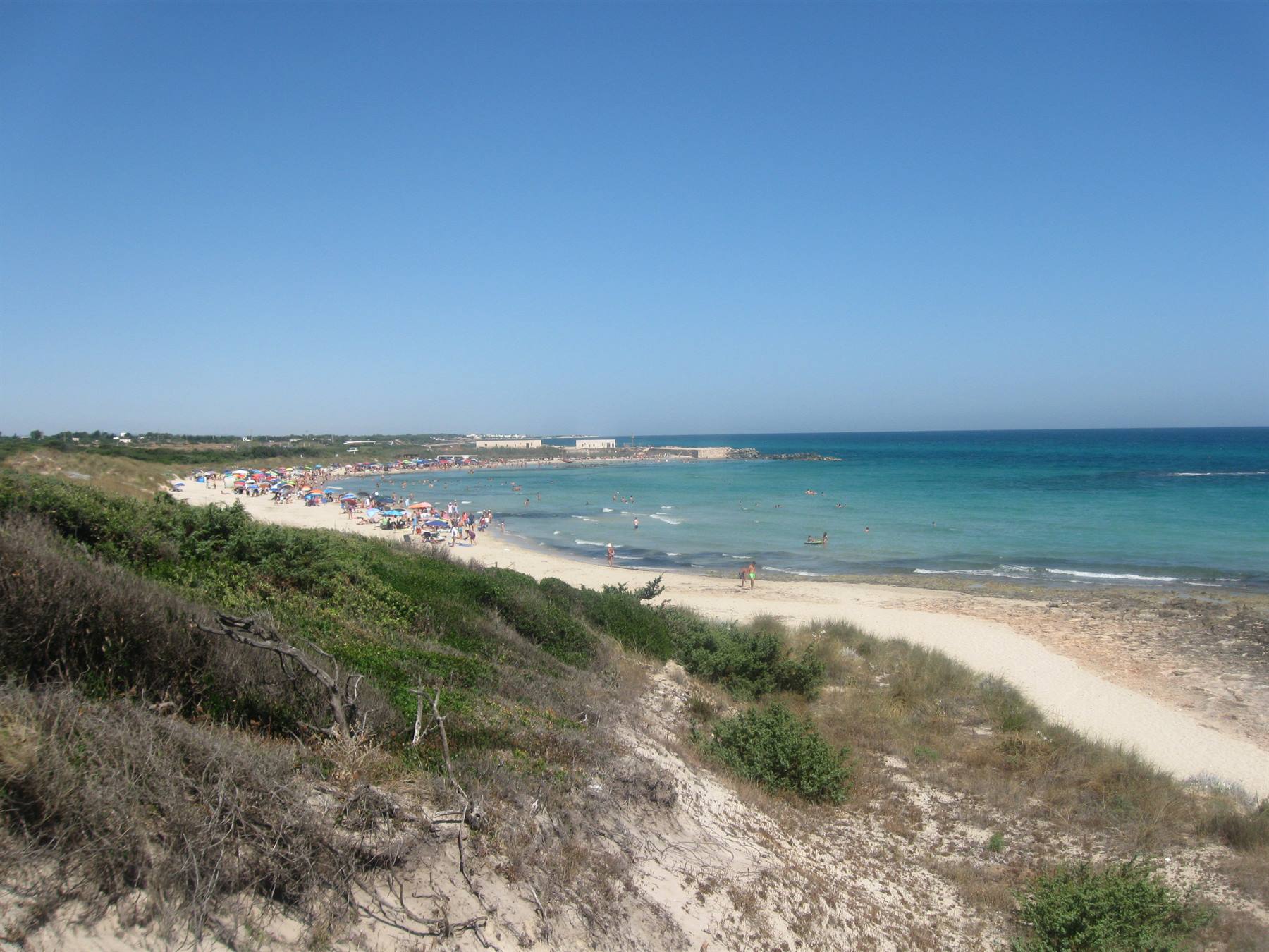 Spiaggia sabbiosa con ombrelloni e bagnanti, macchia mediterranea e mare turchese