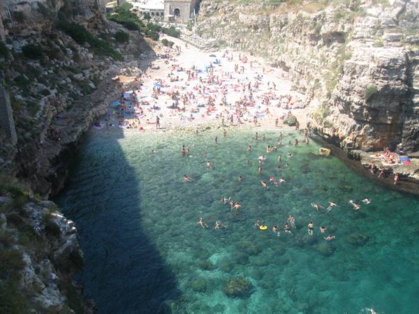 Swimmers in turquoise water between limestone cliffs, crowded beach under the sun