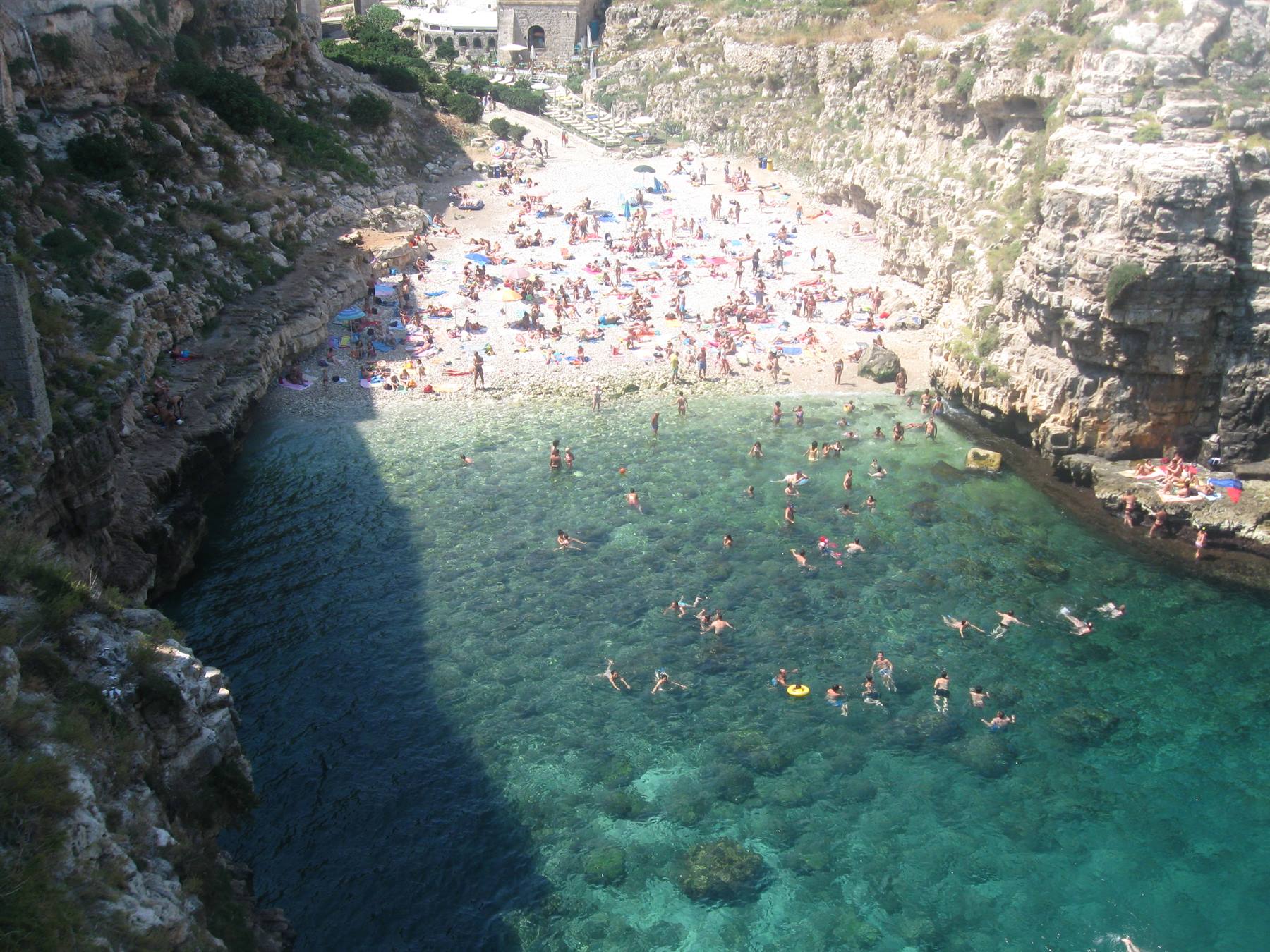 Bagnanti nelle acque turchesi tra scogliere calcaree, spiaggia affollata sotto il sole