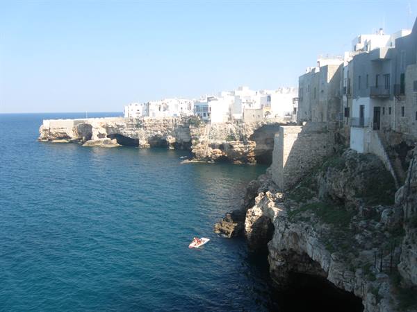 White houses of Polignano a Mare on limestone cliffs, small boat on blue sea