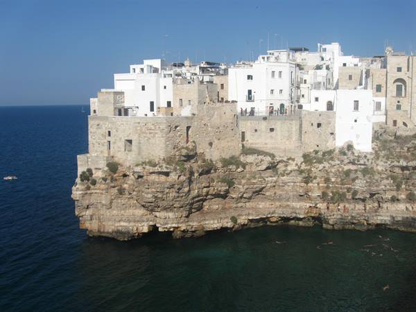 White houses on limestone cliff in Polignano a Mare, blue sea below
