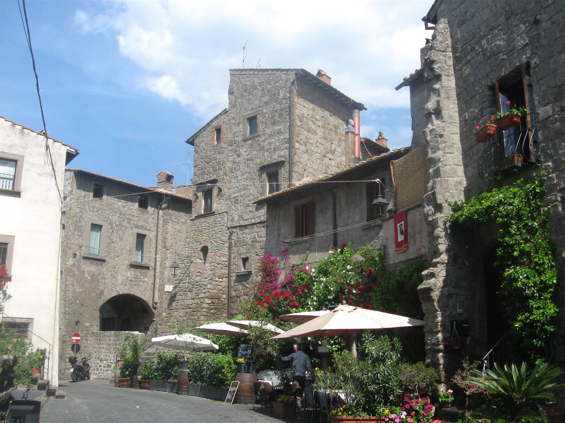 Case medievali in pietra con caffè all'aperto, ombrelloni e fiori nel borgo
