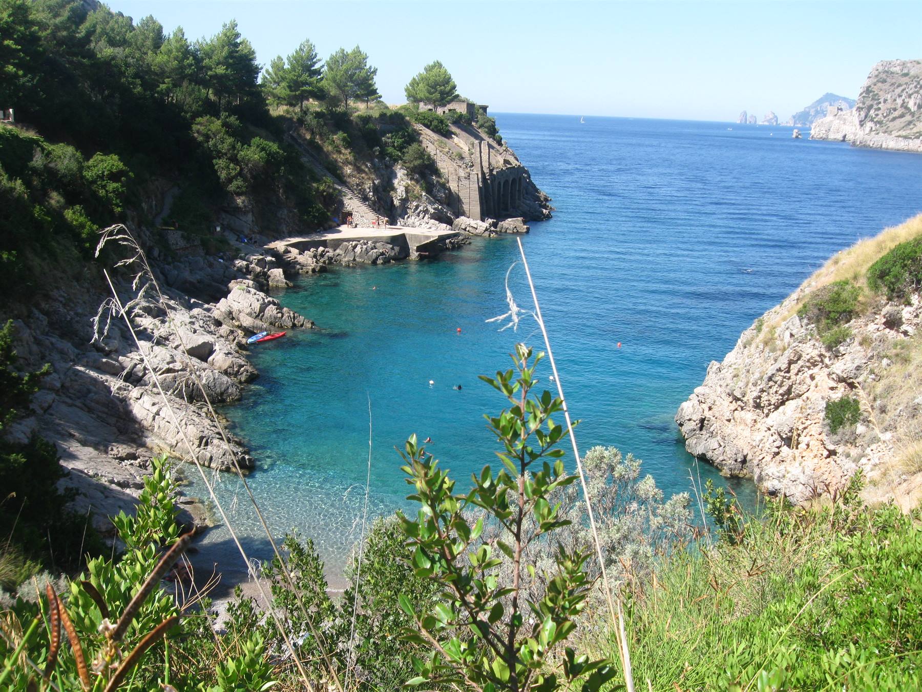 Piccola caletta rocciosa con acqua turchese, scogliera e bagnanti, Capri sullo sfondo