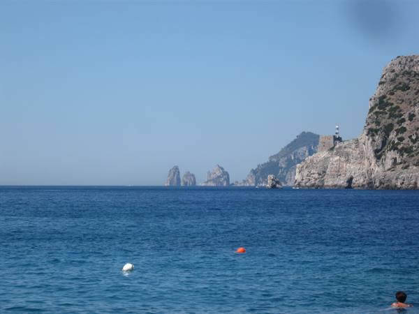 Blue sea with Capri's Faraglioni rocks and a lighthouse on the cliff