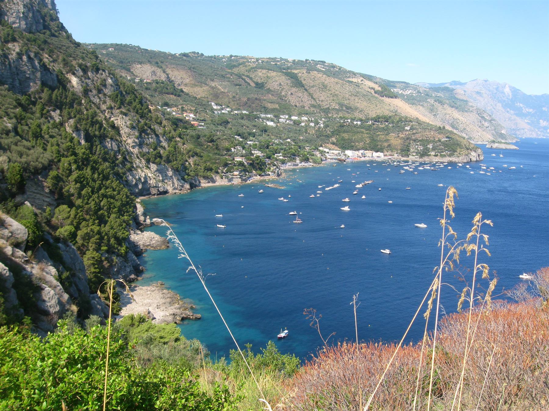Molteplici barche bianche ancorate in una baia blu tra scogliere verdi