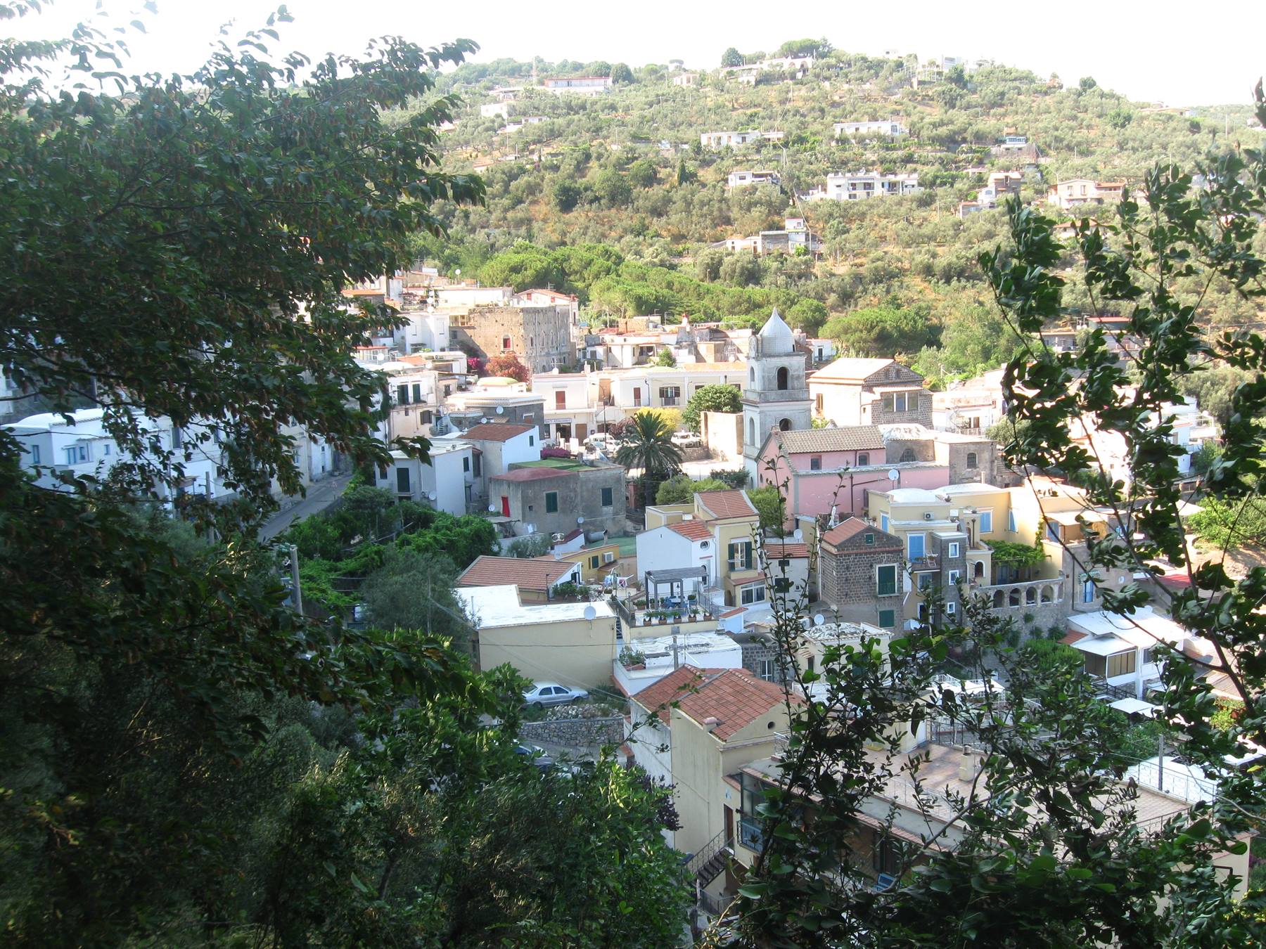 Borgo mediterraneo tra il verde: case colorate, campanile bianco, collina di case sparse