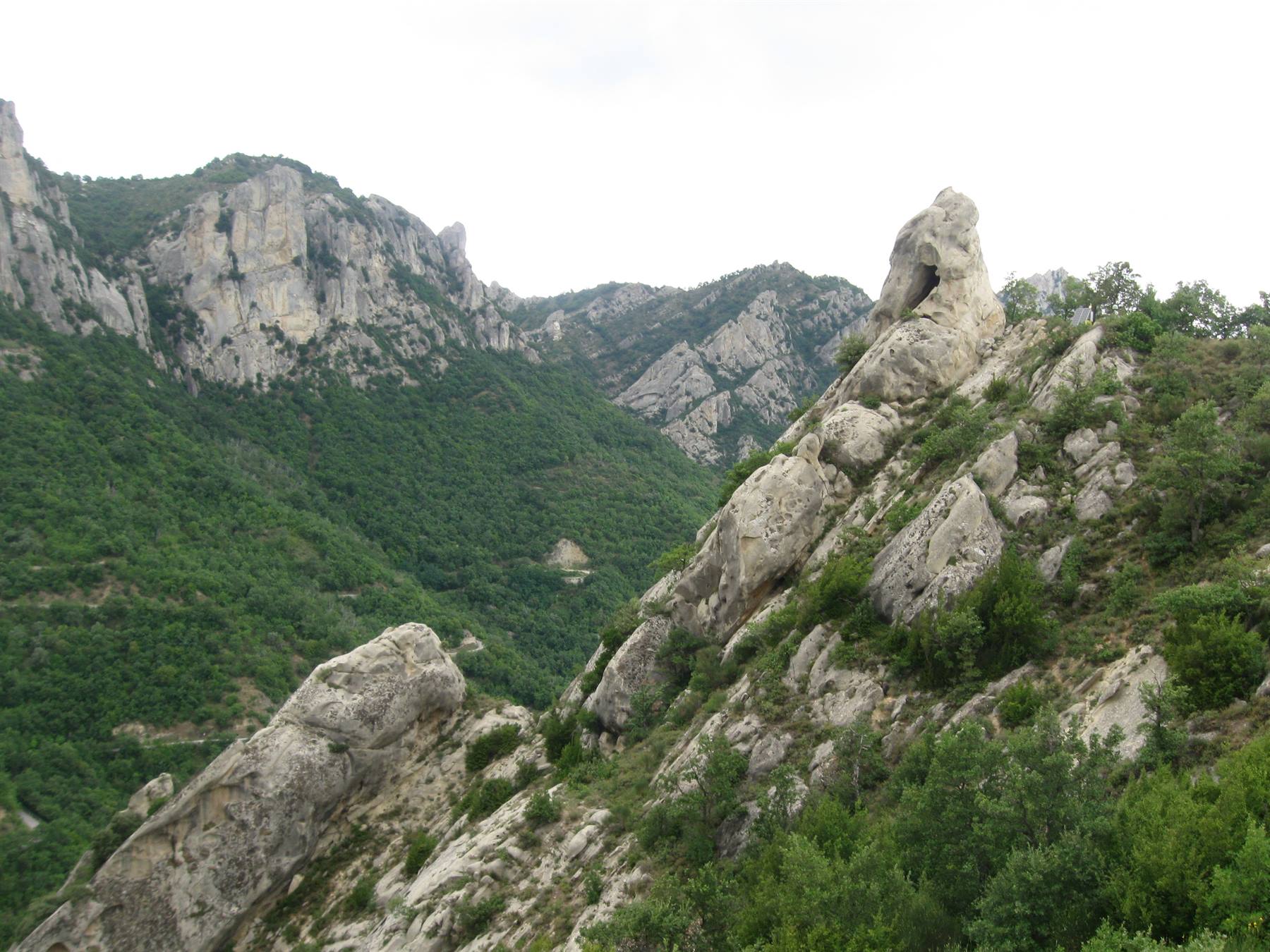 Roccia calcarea con foro naturale sopra versante verde, luce diffusa nuvolosa