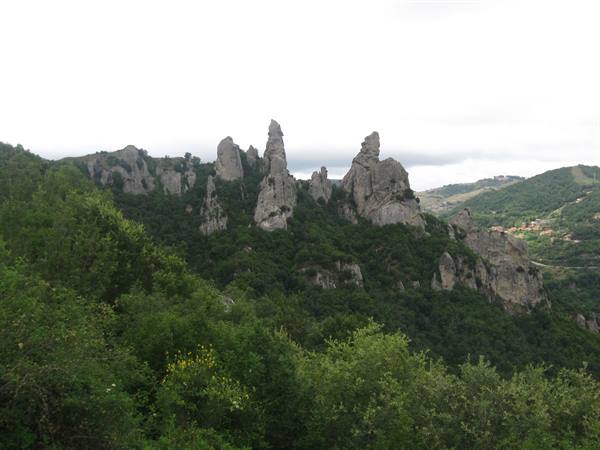Jagged rock pinnacles of the Dolomiti Lucane above green woods, cloudy sky