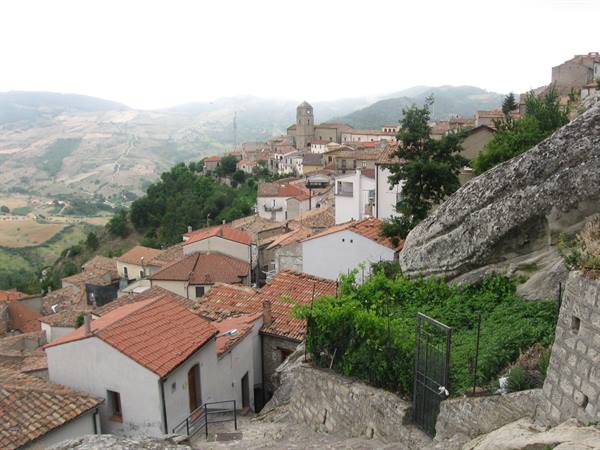 white houses with terracotta roofs below a huge boulder, bell tower over hills