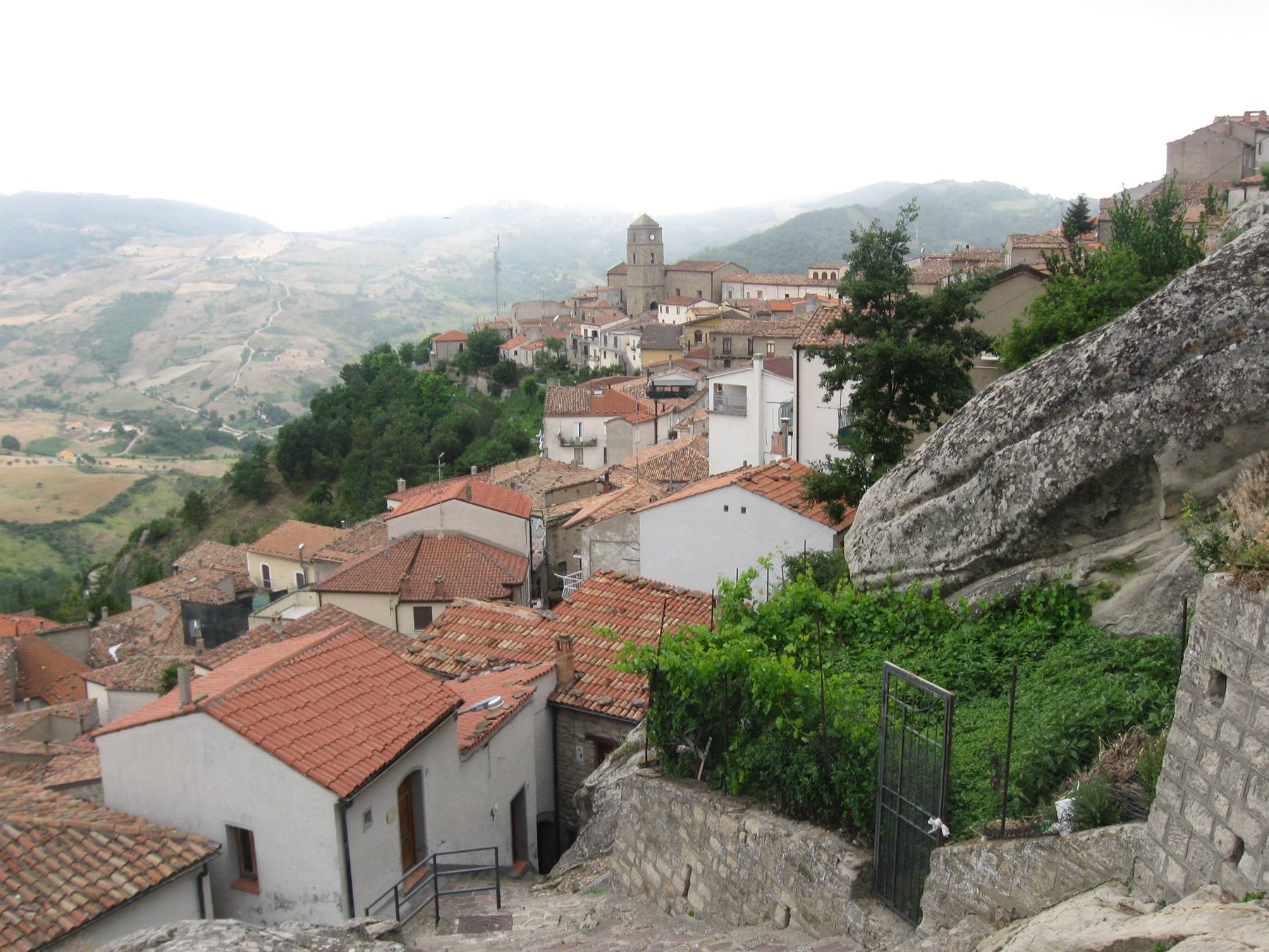 case bianche e tetti di tegole sotto una grande roccia, campanile tra le colline