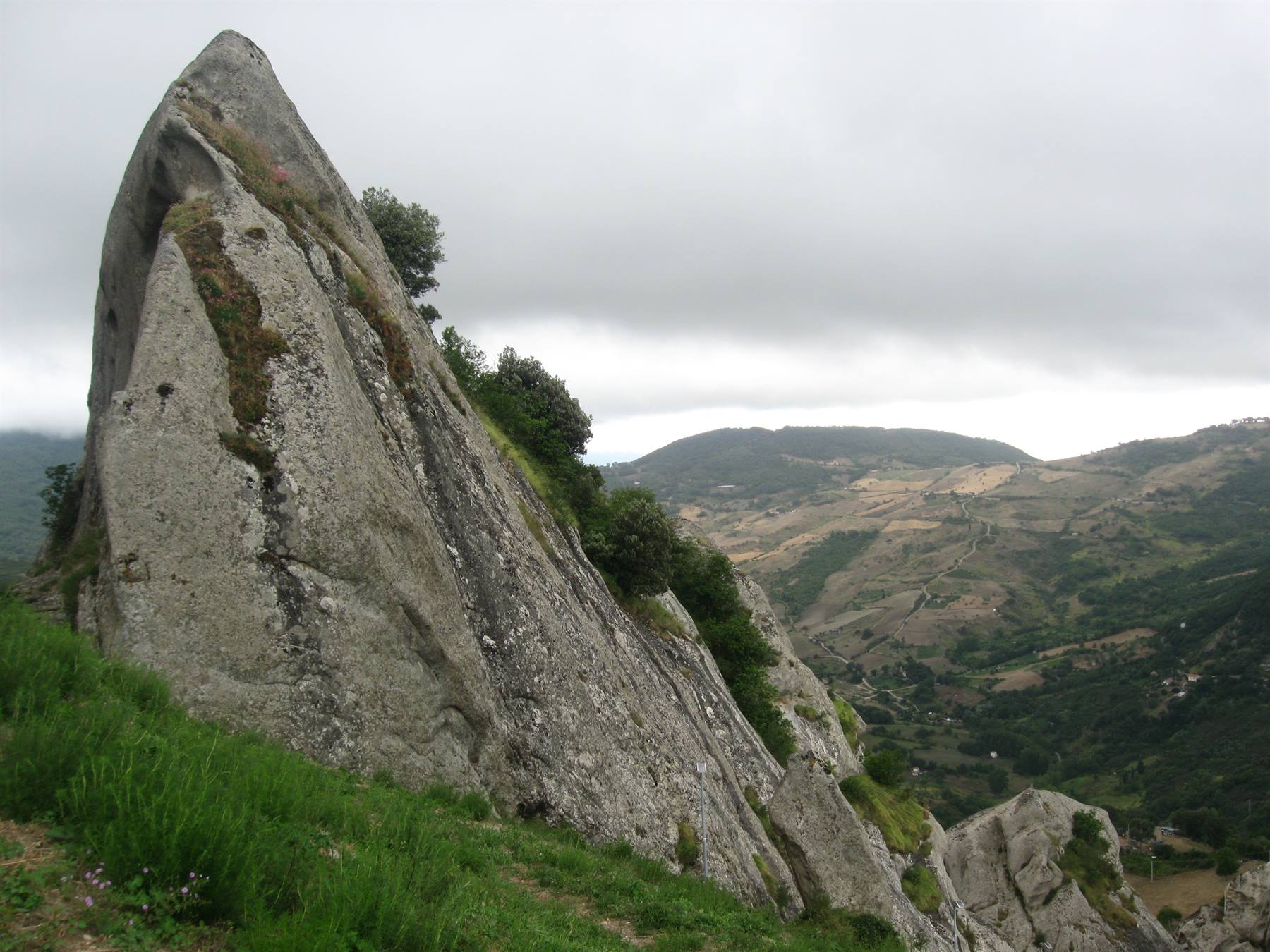 Roccia di granito sporgente sul pendio erboso, colline coltivate sotto il cielo nuvoloso