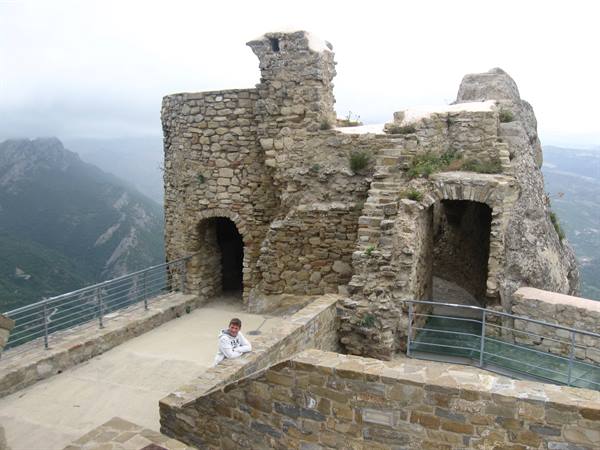 Woman leaning on stone wall of ancient fortress, misty mountains behind