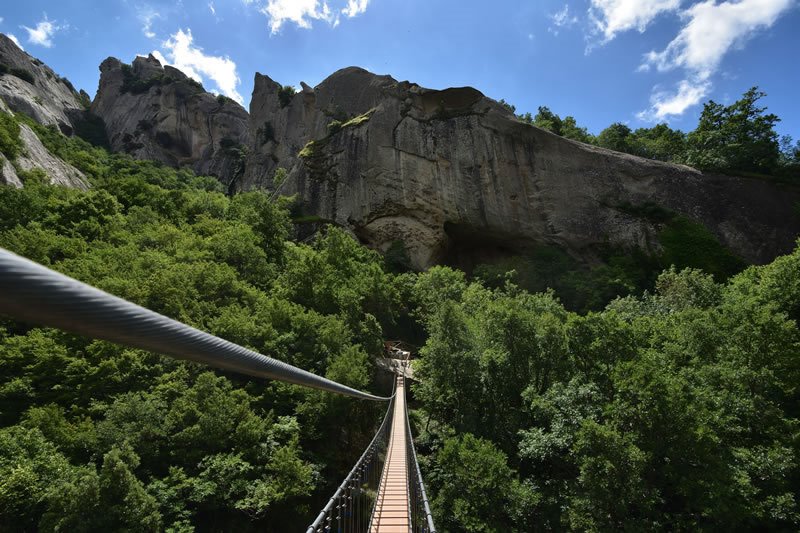 Ponte sospeso in acciaio sul bosco, pareti rocciose sotto il sole