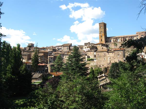 Medieval tuff hill town with Romanesque bell tower, clustered houses among green trees