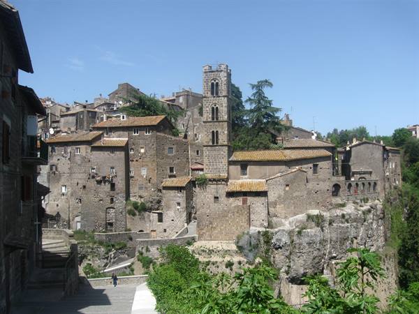 Vitorchiano: tuff houses on the cliff, Romanesque bell tower, stairway under blue sky