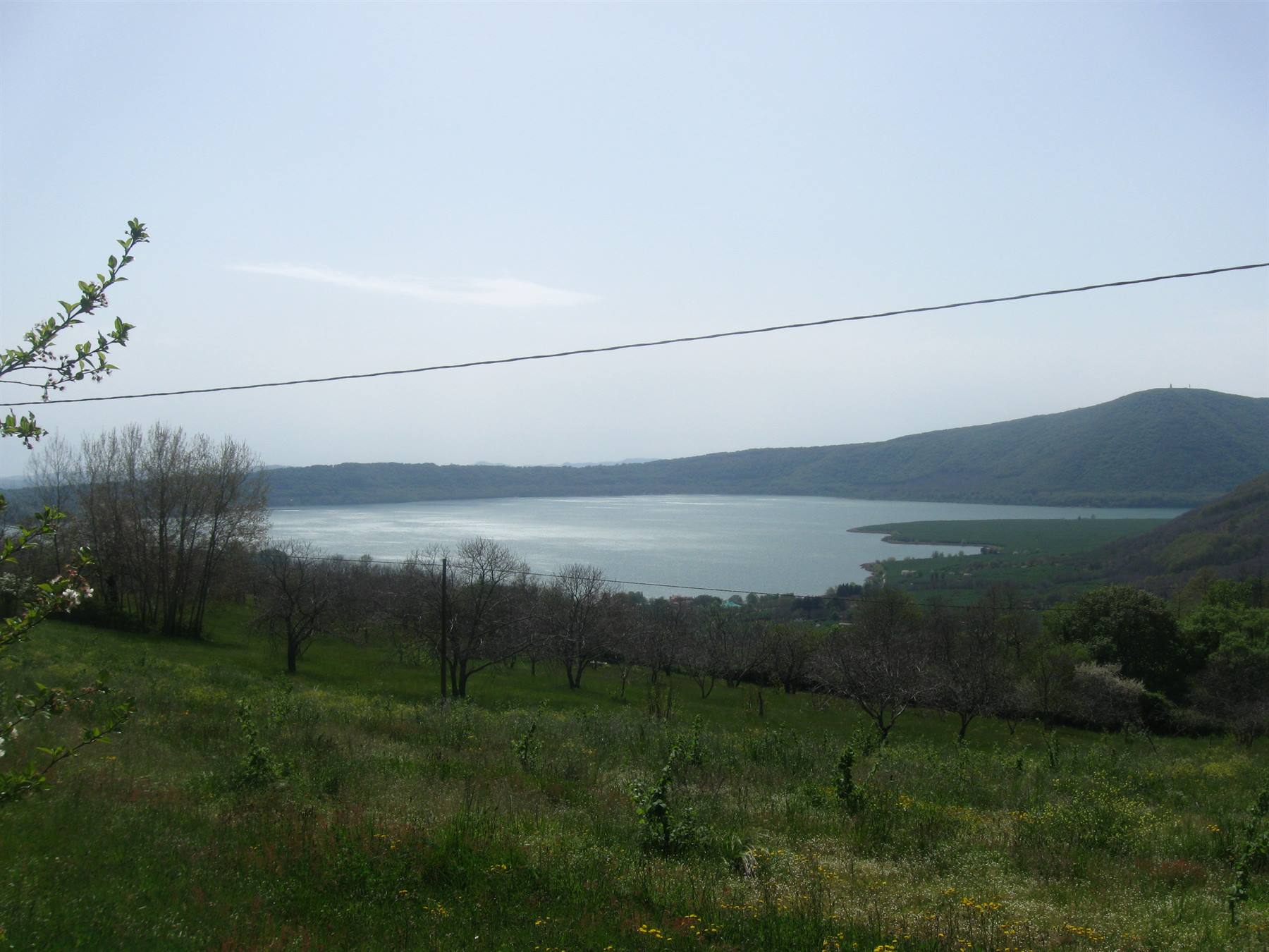 Lago Albano visto dal prato verde sopra, colline e filo elettrico in luce diurna