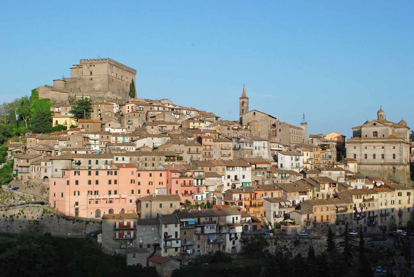 Borgo arroccato con castello in pietra e chiese sotto cielo azzurro