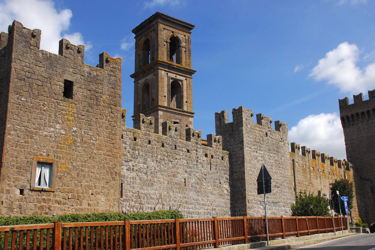 Mura medievali di pietra con merlature e campanile, Viterbo, sotto cielo azzurro