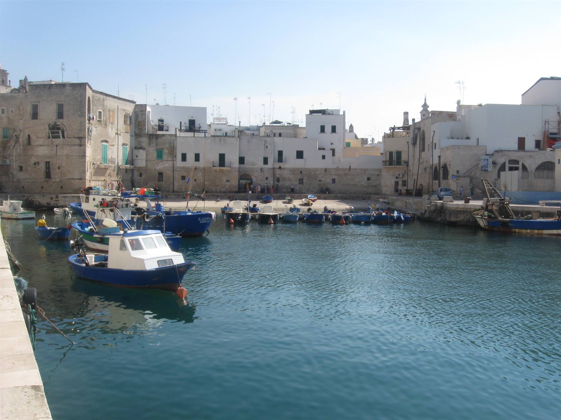 Barche blu nel porto vecchio di Monopoli tra case bianche illuminate dal sole