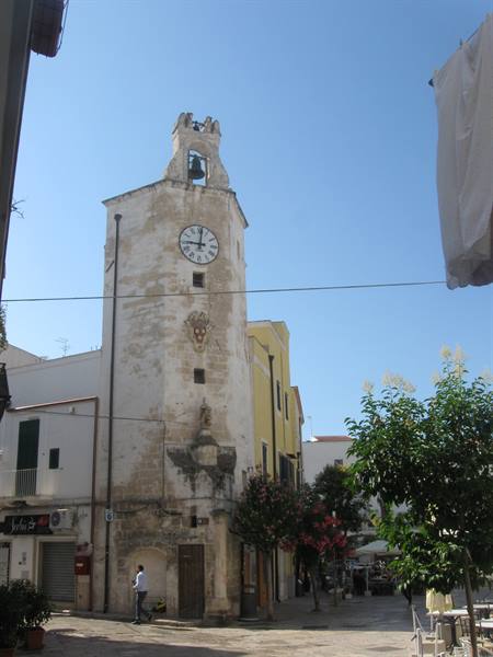 Stone clock tower with bell chamber, sunny town square with trees