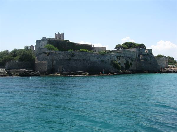 Ancient stone fortress on the island, ramparts above turquoise sea, person fishing on rocks