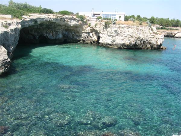 Limestone cove with cave, clear turquoise water, white villa above the rocks