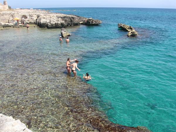 Swimmers in clear turquoise water over limestone rocks, Salento coast