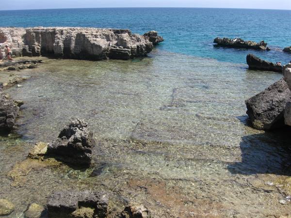 Limestone rock pool with crystal-clear water, grey boulders and blue sea