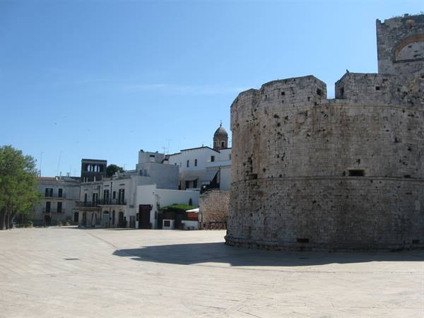 Stone bastion of Conversano castle beside whitewashed houses under blue sky