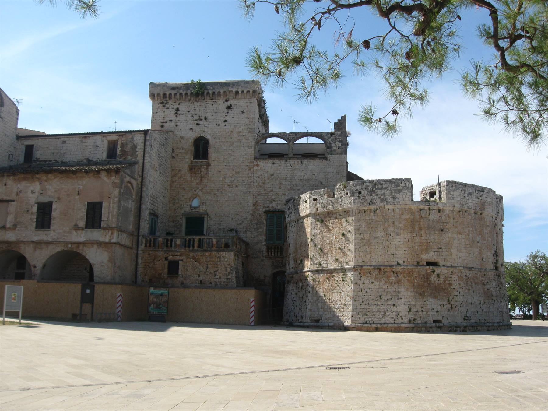 Castello di Conversano: torre circolare in pietra e palazzo medievale sotto rami di pino