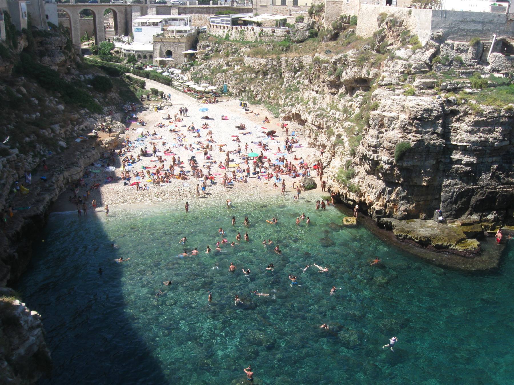 Bagnanti nella cala di Lama Monachile a Polignano a Mare, scogliera calcarea e acqua turchese