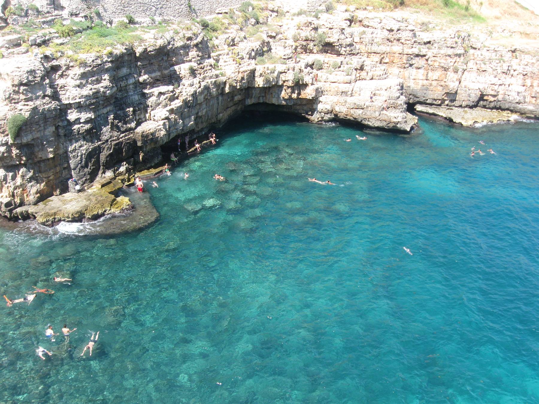 Nuotatori in acqua turchese sotto scogliere calcaree di Polignano a Mare