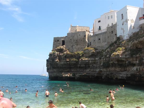 Swimmers in turquoise water beneath the white houses of Polignano a Mare