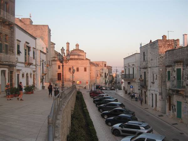 Stone square with white buildings, domed church, parked cars, golden evening light
