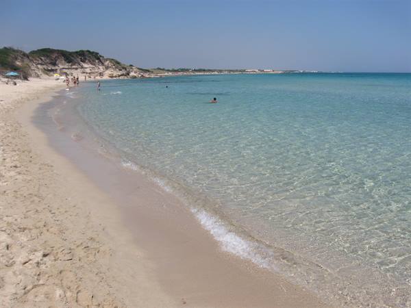 White sand beach with clear turquoise water, swimmers bathing in the sunshine