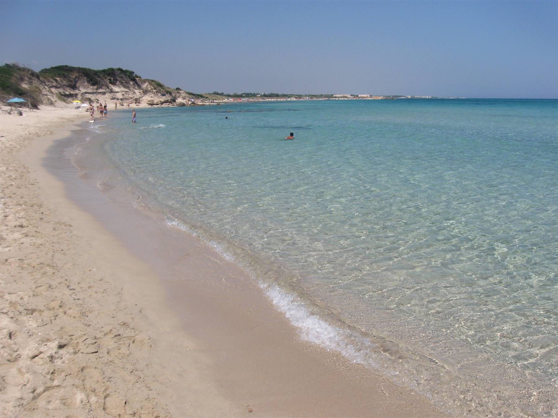 Spiaggia di sabbia chiara con acqua turchese trasparente, bagnanti nuotano sotto il sole