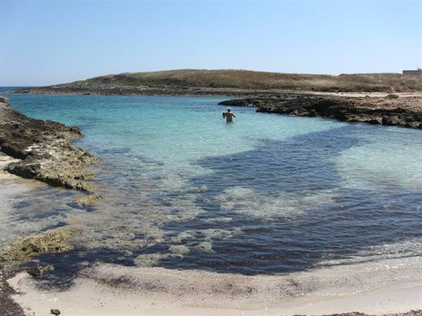 Limestone cove with turquoise water, sandy seabed, one swimmer wading