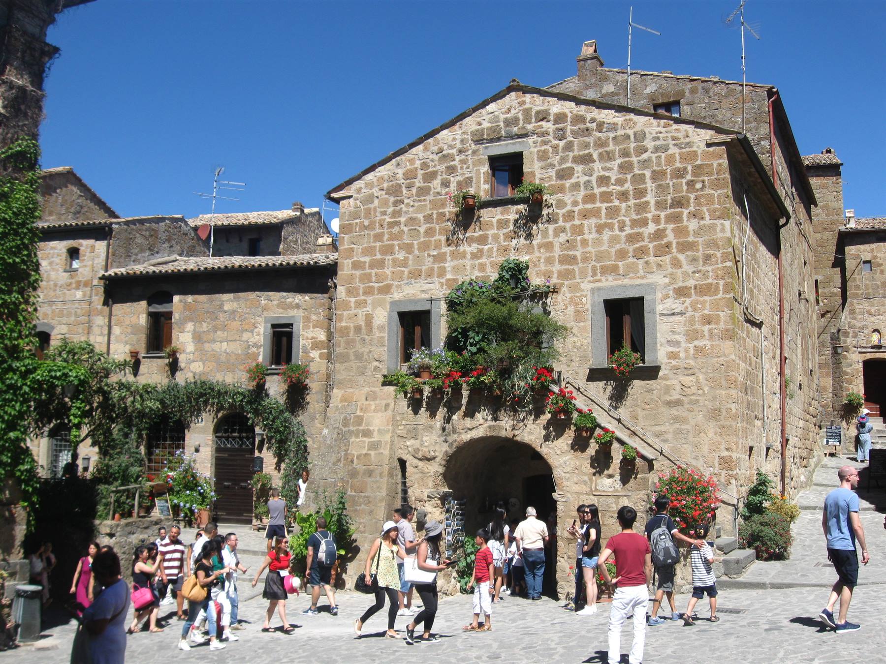 Turisti sulla piazza in pietra davanti alle case di tufo fiorite di Civita di Bagnoregio