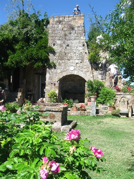 Tourist atop a medieval stone tower with arch, blooming garden below
