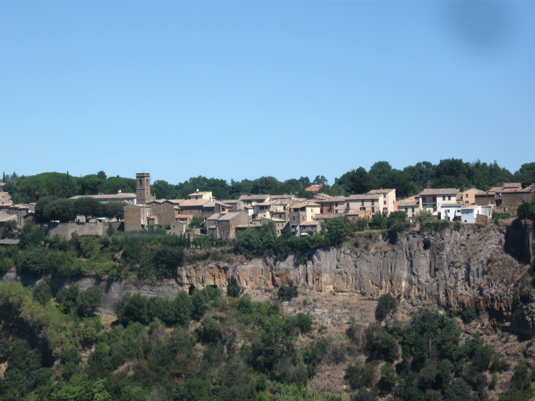 Borgo di case in pietra e campanile sul bordo di una rupe tufacea al sole