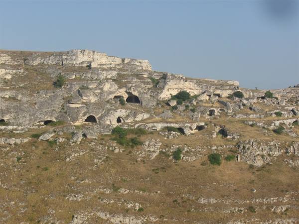 Cave dwellings carved into limestone hillside beneath a clear blue sky, Matera