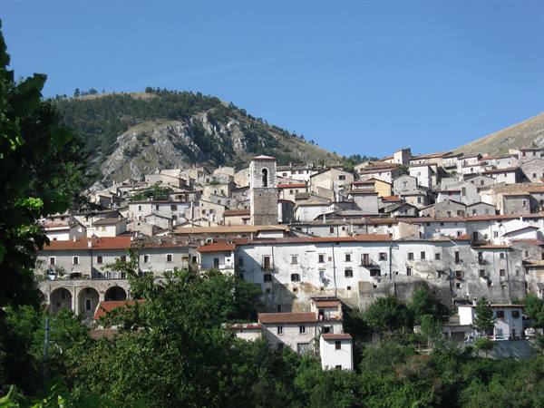 Hillside village of stacked stone houses, central bell tower, clear blue sky