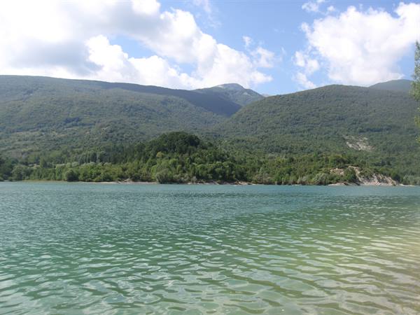 Green lake among forested hills under cloudy sky, daylight